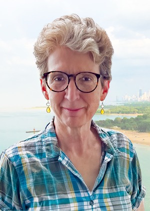 professor wearing a blue and green plaid button up shirt in front of a forested backdrop